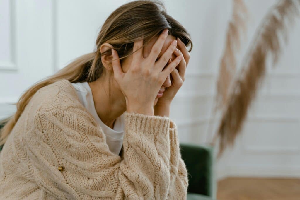 A woman sitting indoors covering her face in frustration, depicting stress and mental health challenges, and a narcissist target.