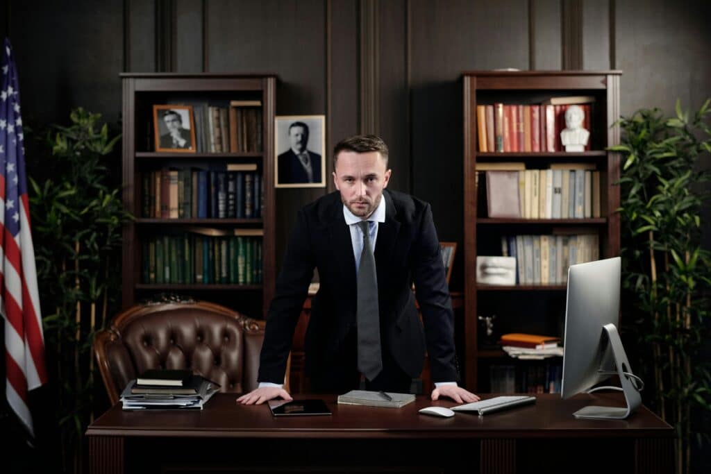 Confident narcissistic boss businessman standing at desk with USA flag in office library.