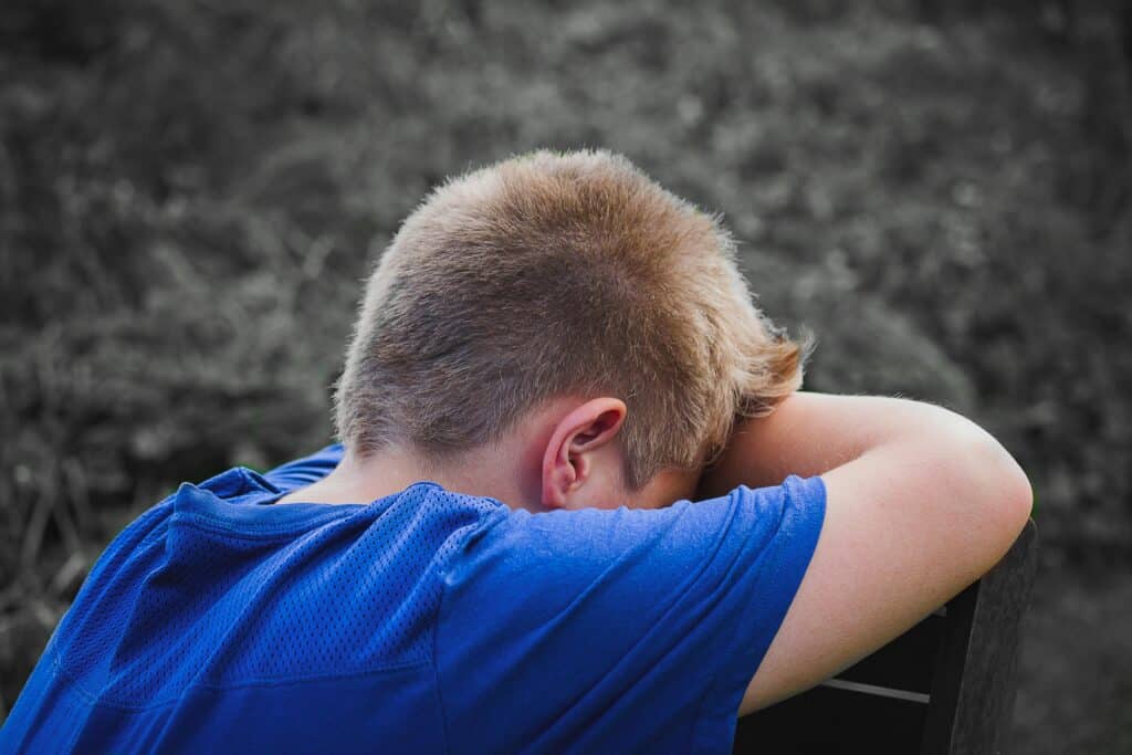A young boy in a blue shirt rests is sad due to emotional abuse and needs help with narcissistic abuse recovery.