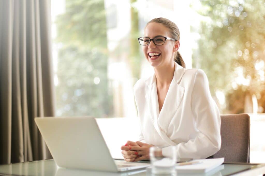 Cheerful businesswoman in glasses working on a laptop, symbolizing better self esteem from working with a therapist for entrepreneurs & business owners.
