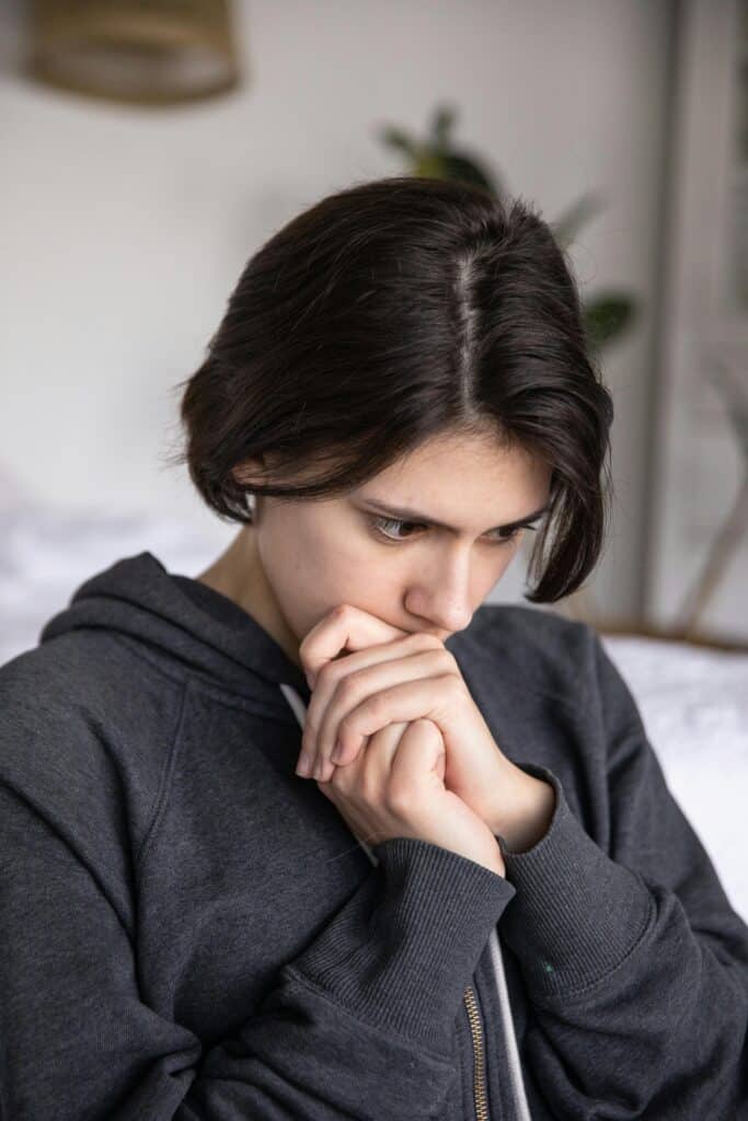 A thoughtful young woman with short hair wearing a hoodie and jacket, sitting indoors.