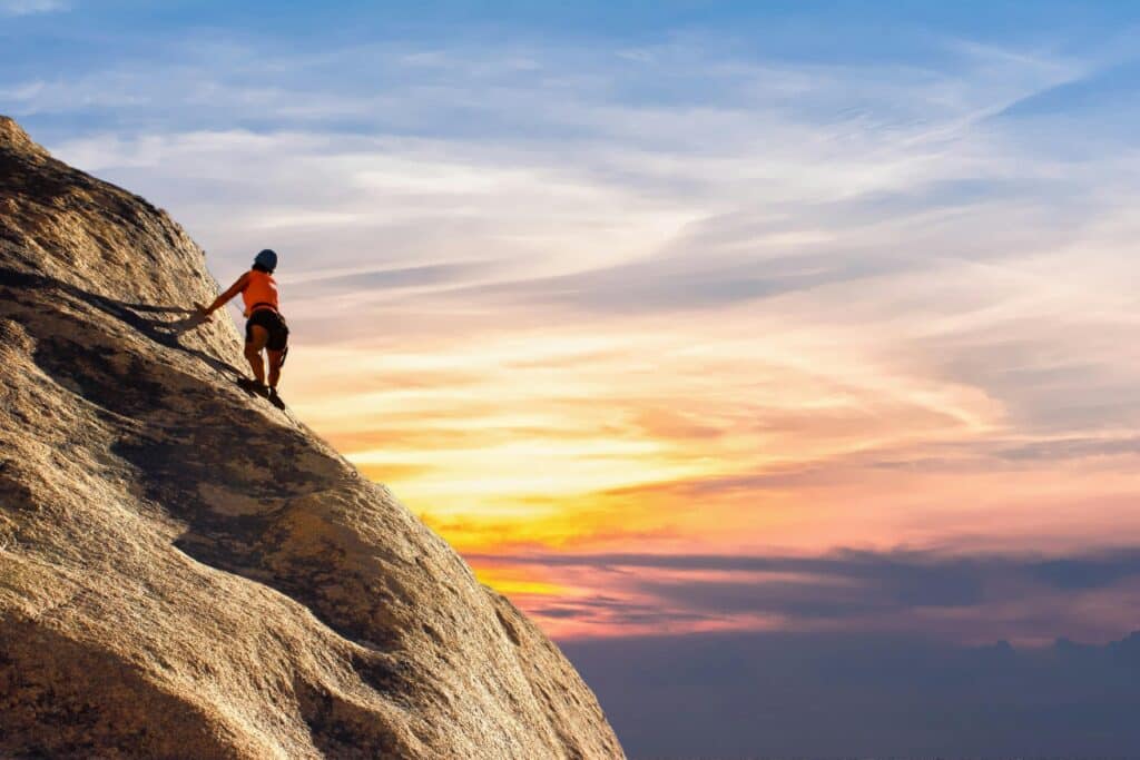 Climber conquers rock face at sunset, embracing the thrill and challenge which symbolizes the challenges of business ownership