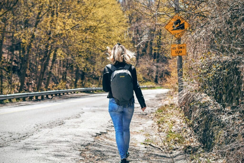 A woman with a backpack walks along a scenic forest road in spring, enjoying an outdoor hike.