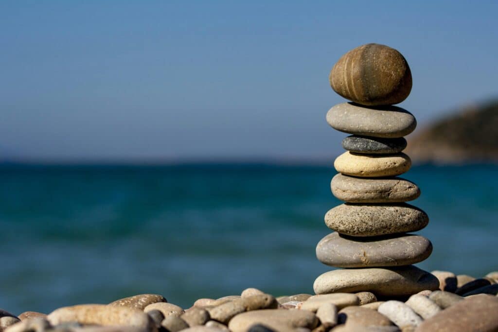 Nervous system reset with a calming strategy 54321 symbolized by the stack of balanced stones on a beach with a tranquil ocean backdrop for meditation and zen.