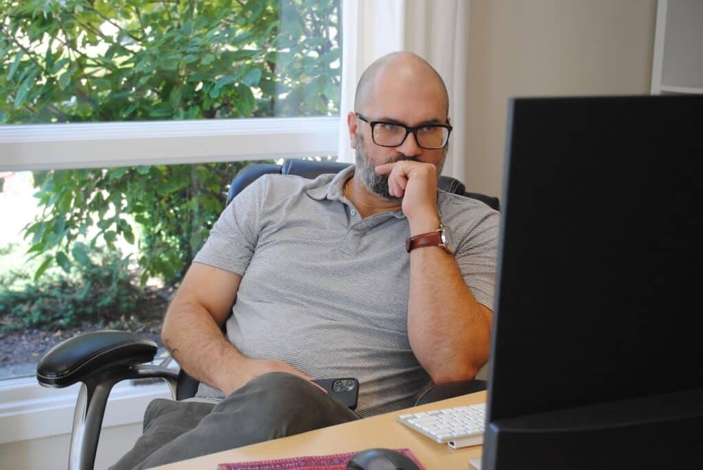 Man at home quietly thinking about going for counselling -for stress and mental load, showing how workplace mental load follows men into home life.