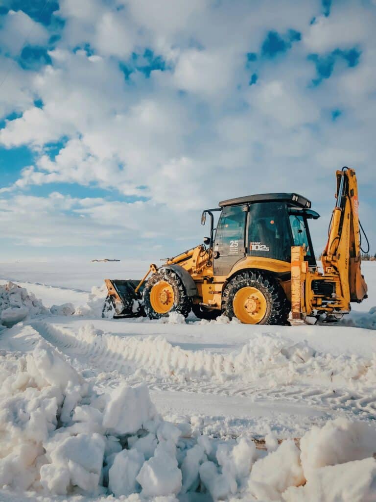 A yellow bulldozer clearing snow under a bright blue sky with clouds, showcasing winter machinery.