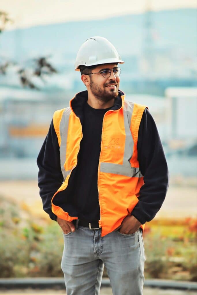 Smiling construction worker wearing safety vest and helmet on a construction site.