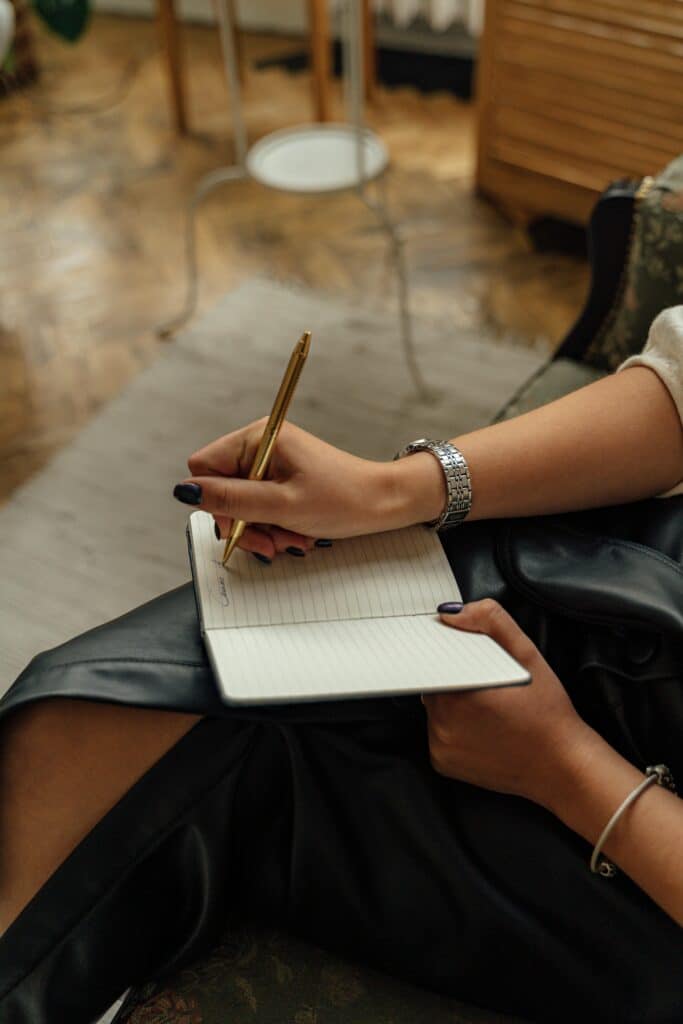 Close-up of hands writing in a notebook with a pen, indoors on a cozy setting.