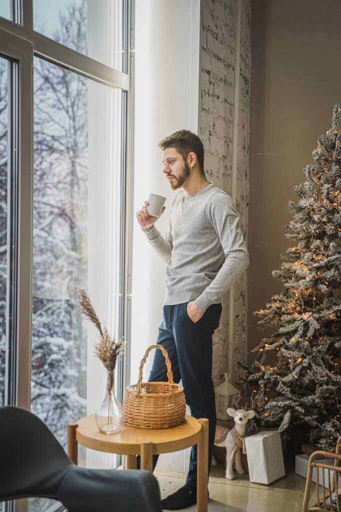Man enjoying coffee next to a Christmas tree, indoors on a winter's day.