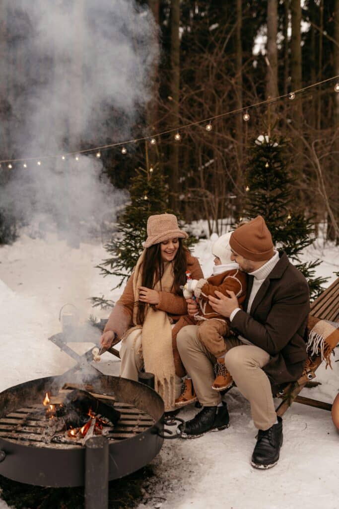 A family enjoys a winter bonfire in a snowy forest setting.