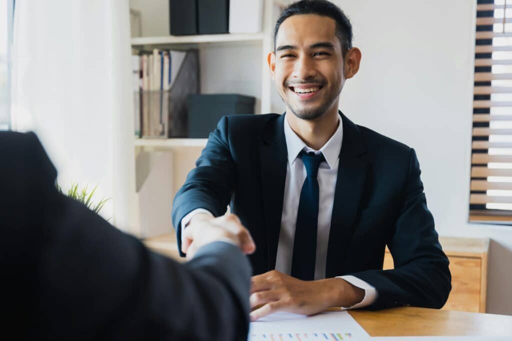 Confident businessman in suit shaking hands at office desk, symbolizing successful high achieving professional