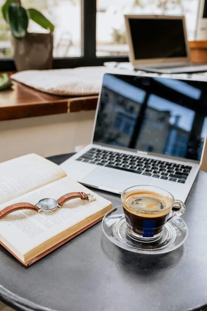 A serene workspace high responsibility professional desk with a laptop, coffee, book, and wristwatch on a table by the window.