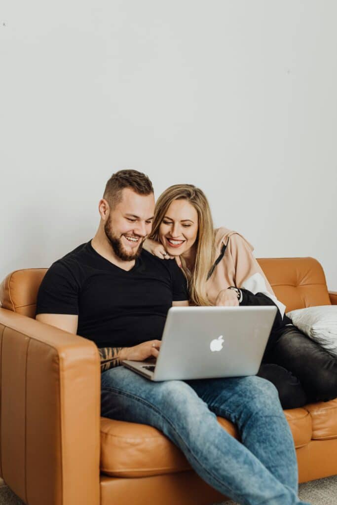 Happy couple sitting on a couch using a laptop, enjoying each other's company indoors.
