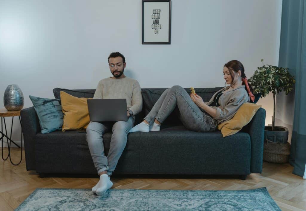 A couple relaxing on a sofa using laptop and smartphone at home. Not talking- symbolizing quiet divorce trend