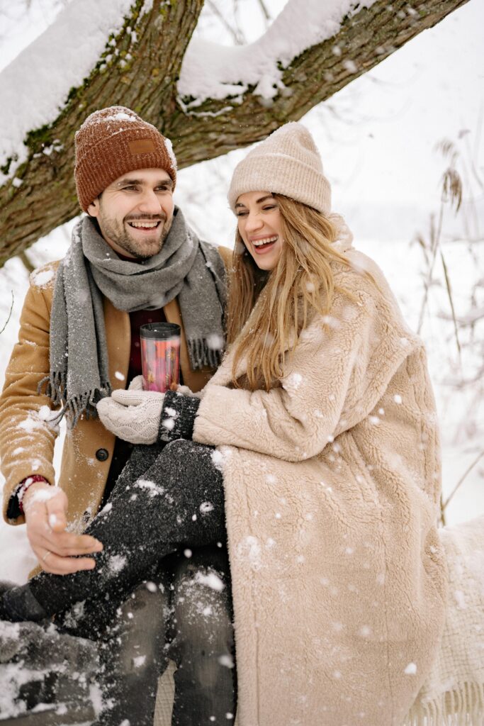 Smiling couple enjoying a snowy day outdoors, dressed warmly in winter clothes.