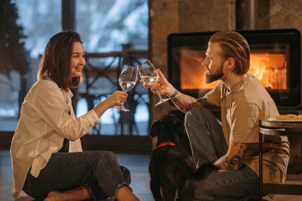 A couple enjoys wine by the fireplace, capturing winter warmth and comfort indoors.
