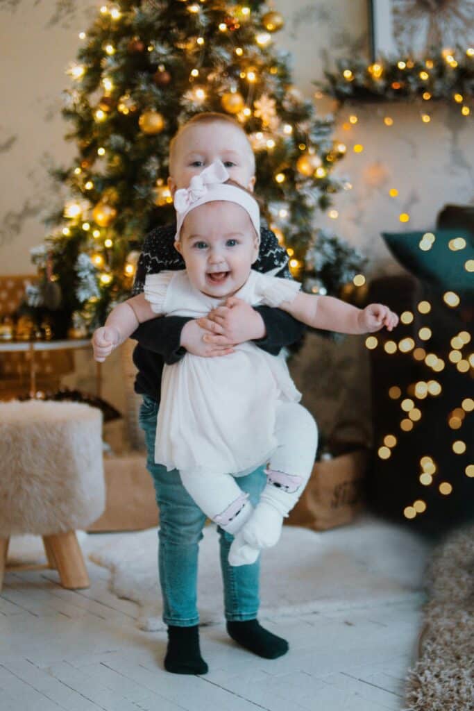 Two happy children standing in a festive room with Christmas decorations and a glowing tree.
