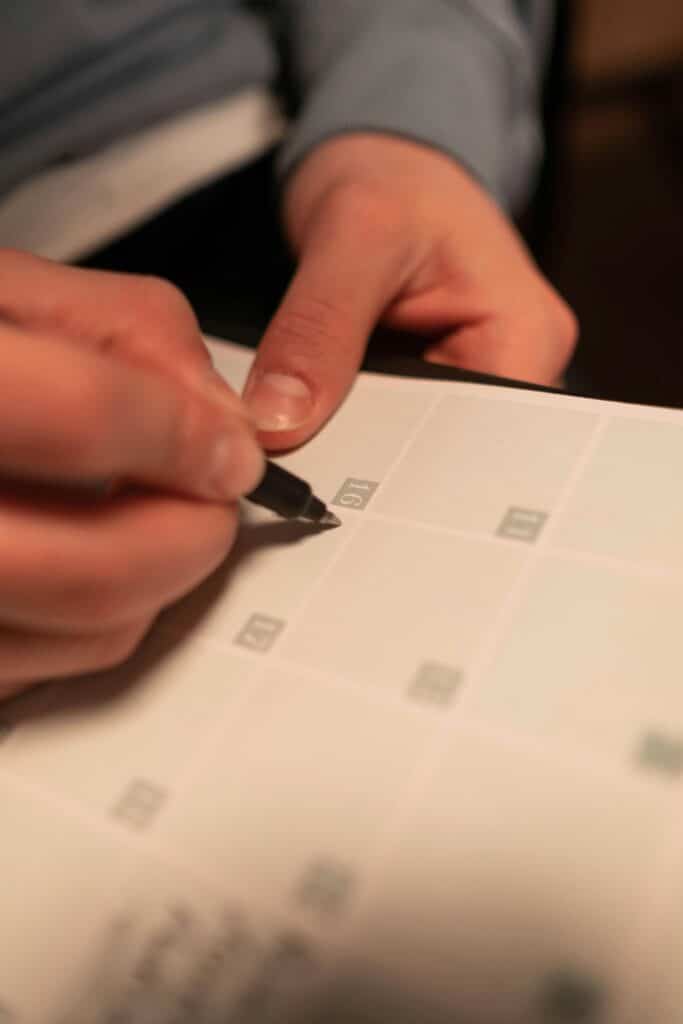 Close-up of a hand writing on a calendar, planning future events such as counsellinfg sessions on communication skills for busy business owners.
