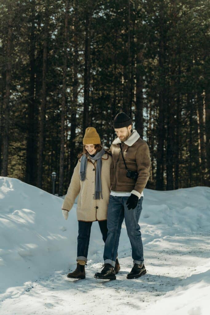 A couple enjoys a peaceful winter walk in a snowy forest, embracing the chilly season.