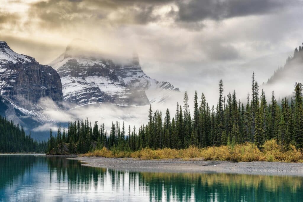 Stunning view of snow-covered mountains reflecting in a serene river in Alberta's and BC winter landscape.