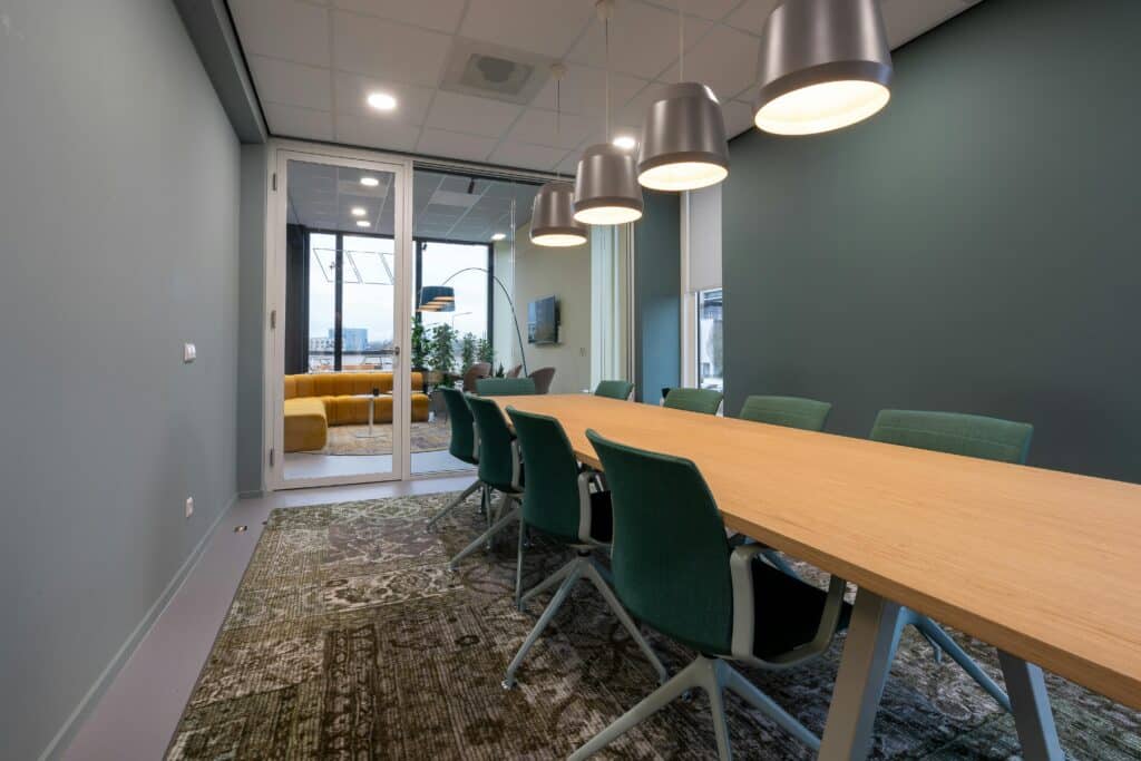 Spacious meeting room with contemporary design, featuring a long table, chairs, and hanging lights.