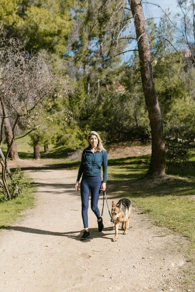 A woman walks her German Shepherd in a scenic forest trail during springtime.