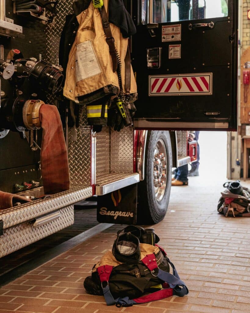 Firefighter gear and equipment beside a parked fire truck in a station house