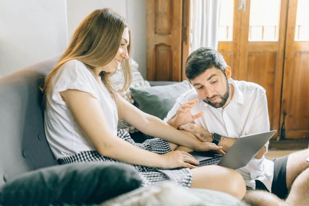 Caucasian couple happily making a video call on a laptop while sitting on a couch indoors.