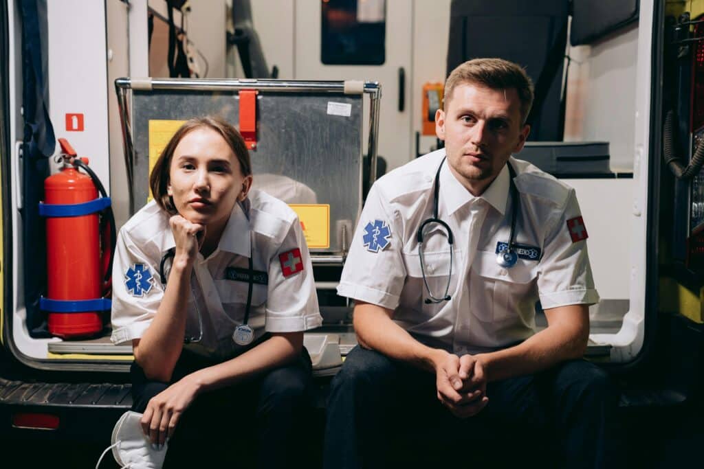 Two paramedics in uniforms sitting inside an ambulance, showcasing teamwork and readiness.