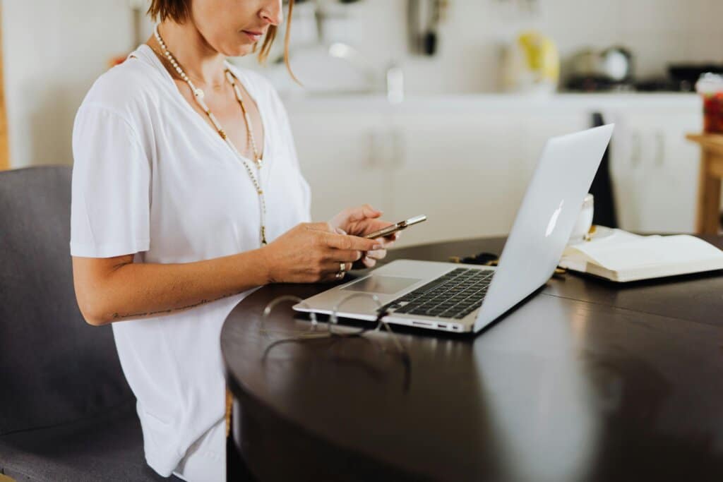 A woman multitasking with her smartphone and laptop in a home office setting.